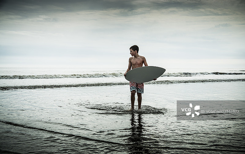 男孩在海浪中玩滑板图片素材