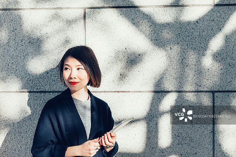 年轻女商人在公园里靠在水泥墙上使用平板电脑图片素材
