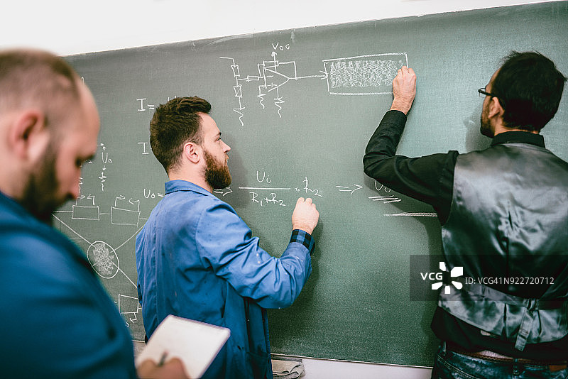 工程师学生在教授和同事面前解决黑板上的电气问题图片素材