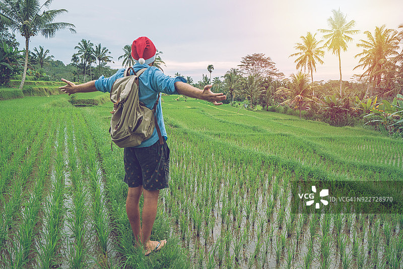 热带气候中的圣诞庆祝活动：在印度尼西亚，男人伸出双臂，戴着圣诞帽图片素材