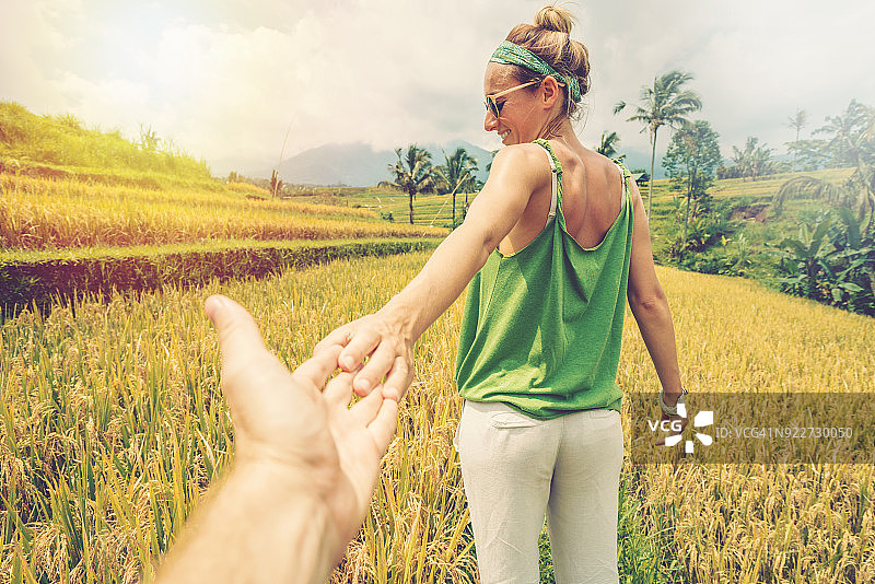“跟我来”概念：年轻女子带领男友走向印度尼西亚巴厘岛乌布的稻田图片素材