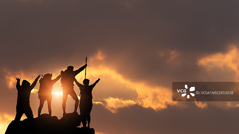 商人和女人们在日落时分在剪影岩石山的山顶上徒步旅行，成功，胜利者和领导者概念。图片素材