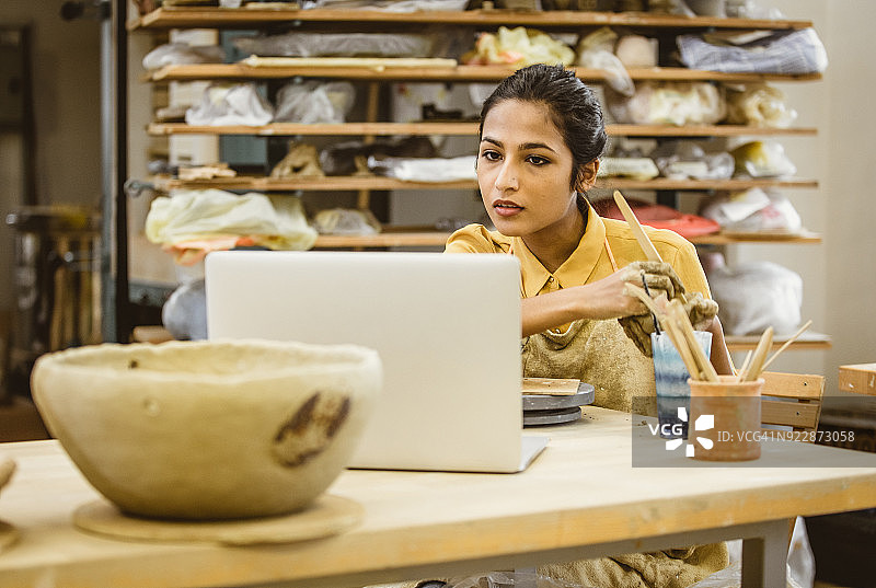 年轻女人制作陶器，使用笔记本电脑图片素材