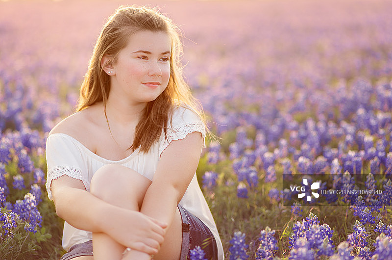 日落时分，青少年女孩在蓝色帽子的田野里的肖像图片素材