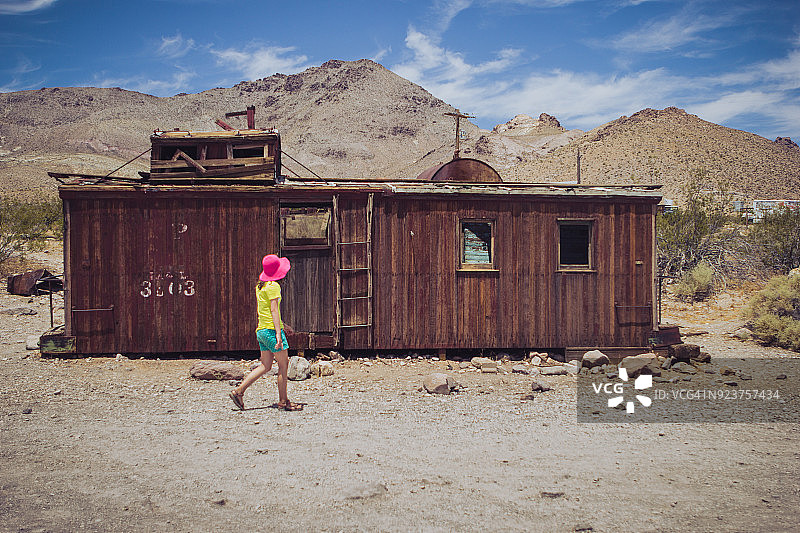 女孩走在内华达州里奥莱特鬼镇的废弃铁路车厢前，戴着粉色帽子和短裤图片素材