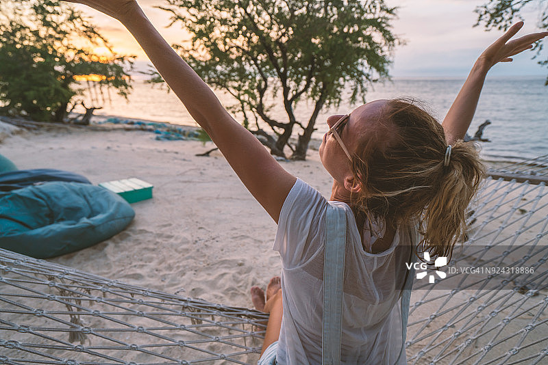 年轻女人在吊床上伸展身体，日落时分图片素材