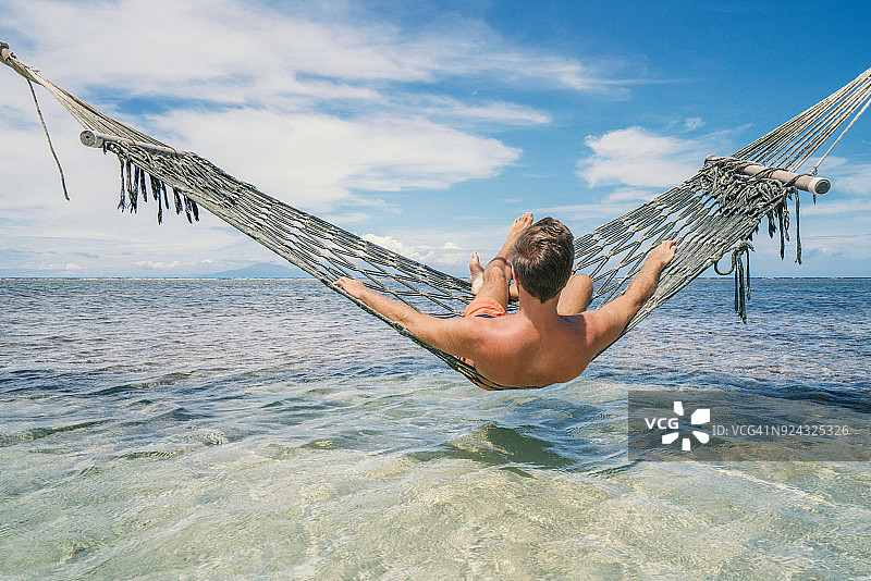 快乐的男人在热带气候的海上吊床上放松图片素材