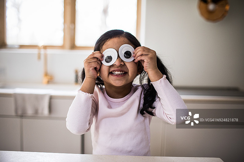 在家玩滑稽的卡通眼睛的年轻女孩图片素材