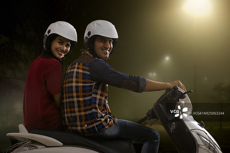夜晚骑摩托车的快乐年轻夫妇图片素材