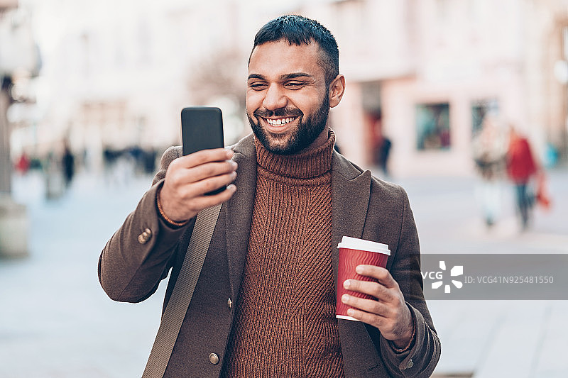 手持智能手机和咖啡杯的微笑青年图片素材