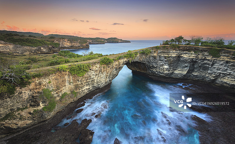 印度尼西亚努沙 Penida Uug海滩海上的石拱门，柔和的色调和温暖的日落图片素材