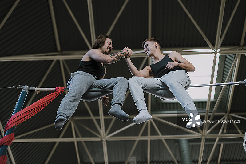 两名微笑的体操运动员坐在高杠上握手图片素材