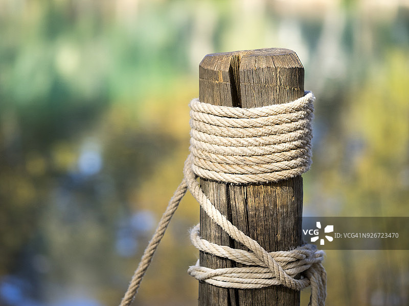 湖岸边系着绳索和绳结的木桩，秋季树叶色彩的倒影，西班牙图片素材