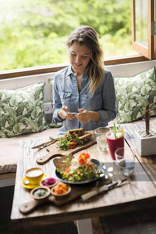 女人在舒适的咖啡馆里用智能手机拍摄食物图片素材