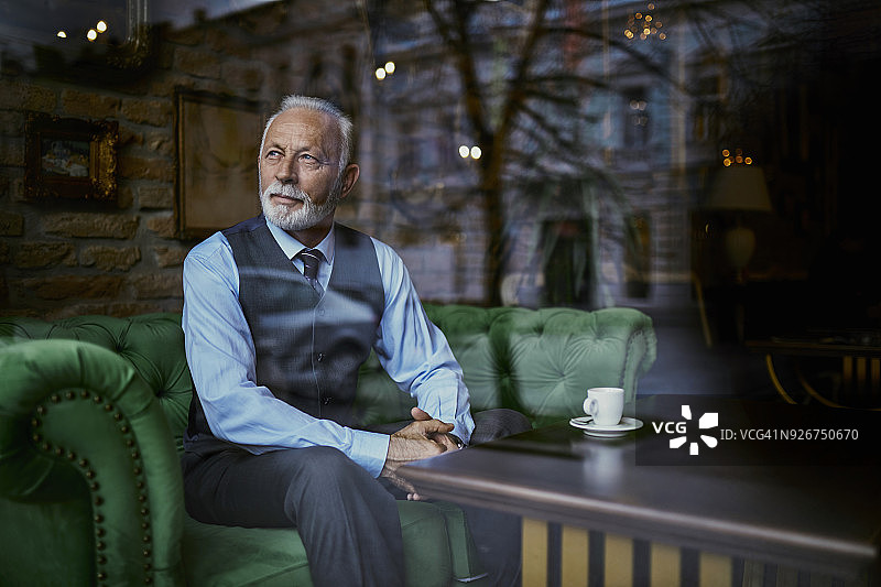 优雅的老年男人坐在咖啡馆的沙发上，望着窗外图片素材