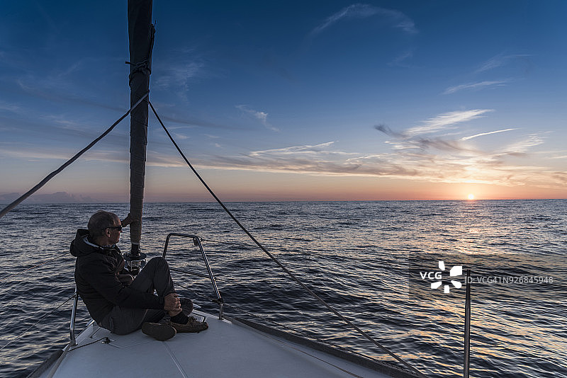 年长的男人坐在游艇上欣赏日落，地点：Porquerolles，普罗旺斯-阿尔卑斯-蓝色海岸图片素材