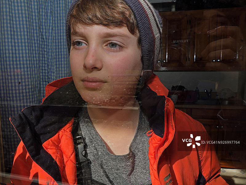 穿着冬季外套和帽子的11岁男孩在乡村的纱门窗户外凝视图片素材