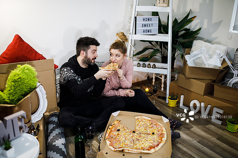 年轻夫妇搬进新家后在地板上享用披萨午餐图片素材