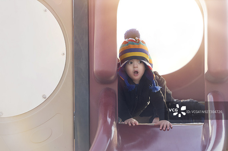 19个月大的异卵双胞胎戴着彩色条纹帽子在滑梯上玩耍图片素材