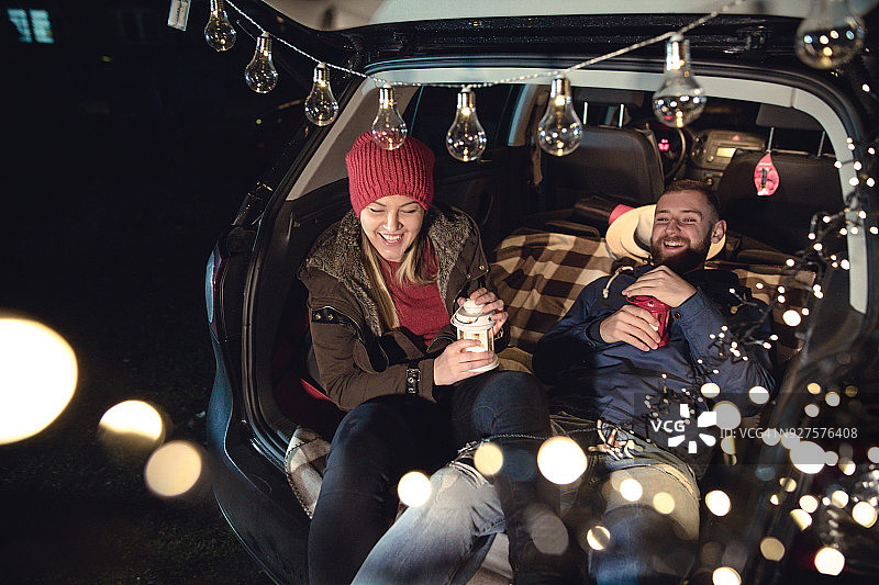 相爱的年轻情侣坐在打开后备箱的汽车里图片素材