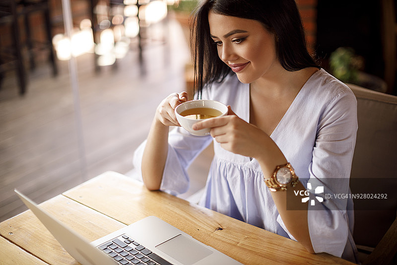 年轻女子边喝茶边在电脑上看邮件图片素材