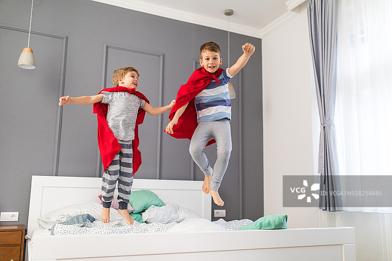 两个顽皮的男孩在床上跳跃，假装是超级英雄图片素材