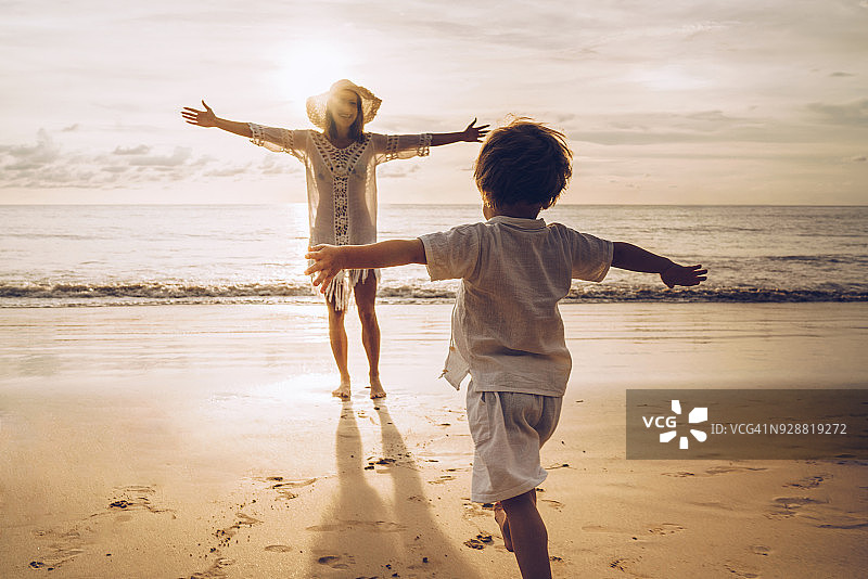 在海滩上奔向母亲怀抱的小男孩的背影图片素材