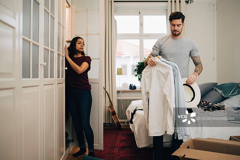 男子在新房里拿着衬衫和帽子站在女子身旁图片素材