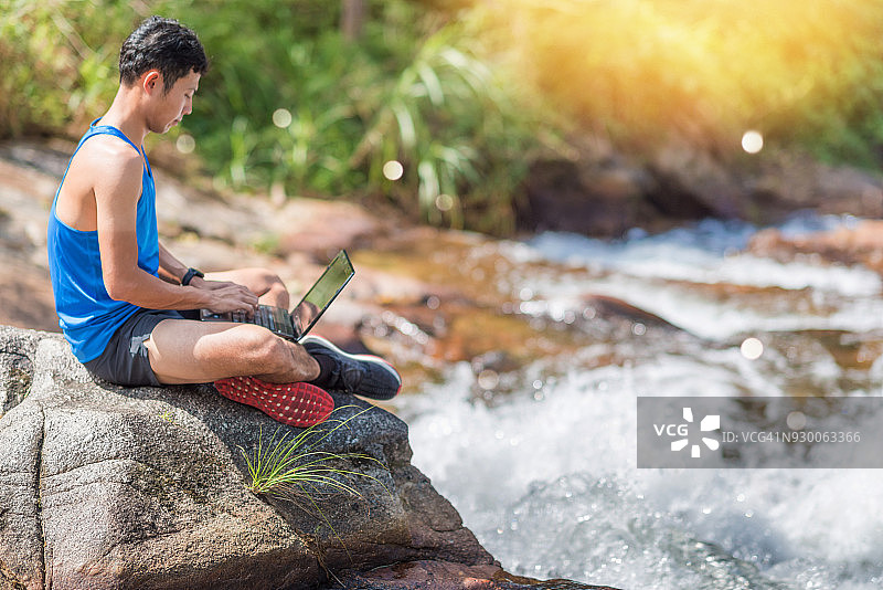 徒步旅行者在森林瀑布边用手机在线工作图片素材