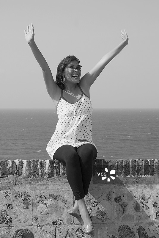 年轻女性坐在边缘，双臂抬起，开心地笑着图片素材