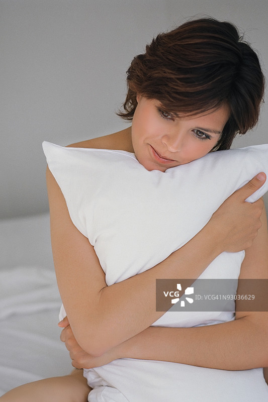 年轻女性抱着枕头坐在床上，墨西哥扎卡特卡斯图片素材