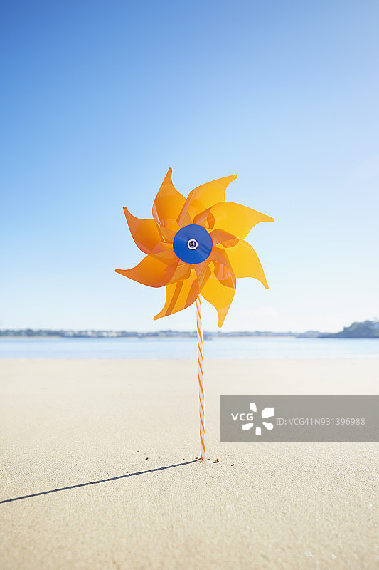 蓝色天空下海滩上的橙色风车图片素材