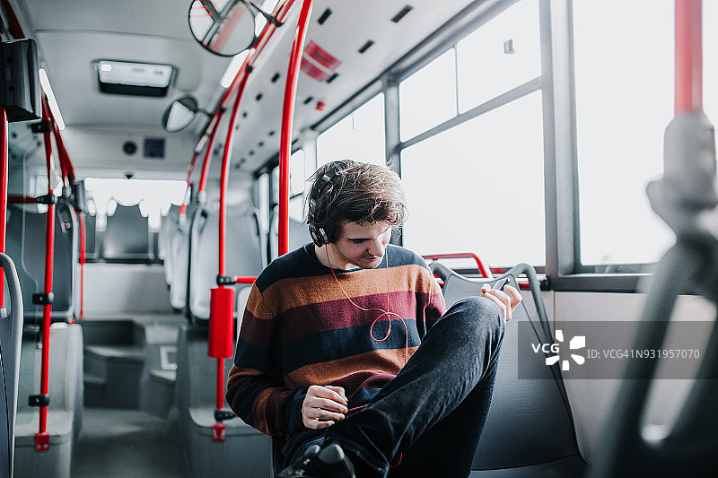 在公共汽车上戴着耳机听音乐的迷人男子图片素材