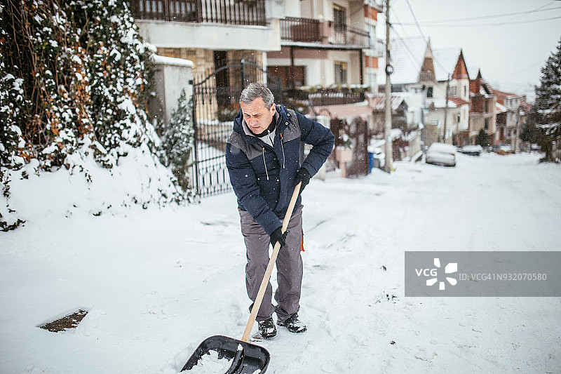 用雪铲清理人行道的年长男人图片素材