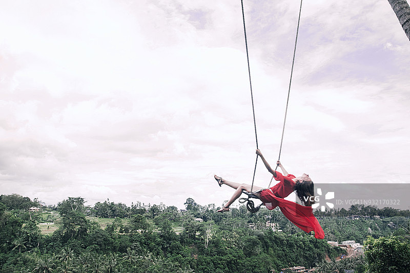 身穿红色连衣裙的女人在巴厘岛丛林中的秋千上飞舞图片素材