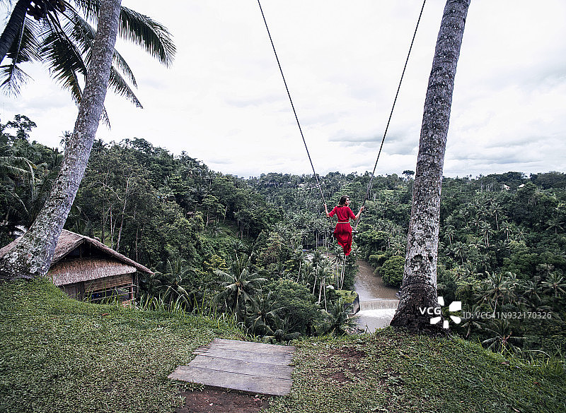 身穿红色连衣裙的女人在巴厘岛丛林中的秋千上飞舞图片素材