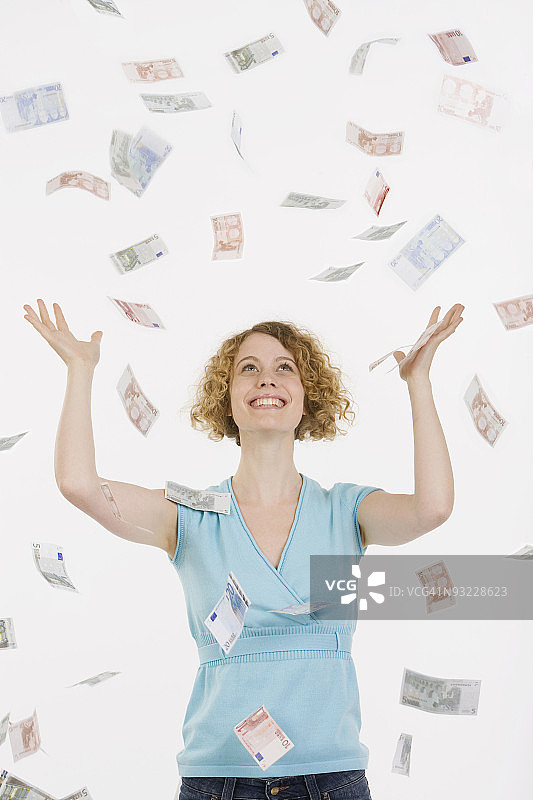 拿着掉落的欧元，面带微笑的年轻女人肖像图片素材