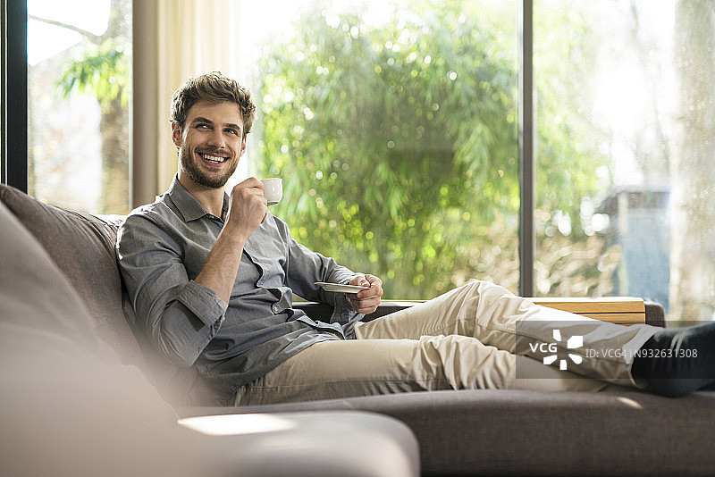 在家里的沙发上放松喝咖啡的快乐男人图片素材