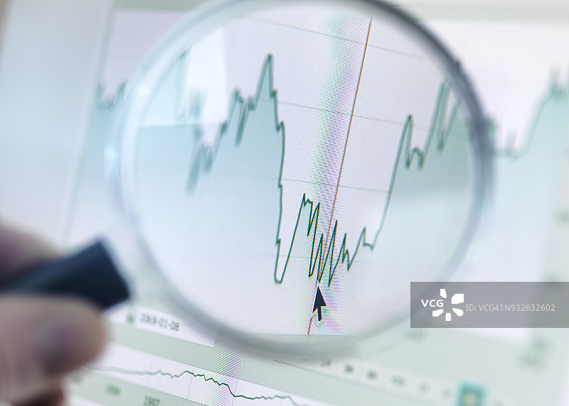 投资者用放大镜分析电脑屏幕上的折线图图片素材