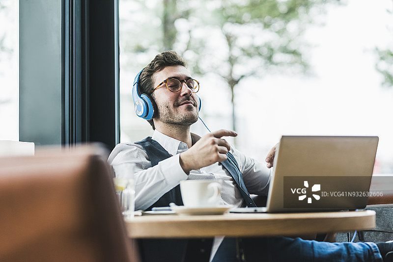 在咖啡馆里使用笔记本电脑和耳机放松的年轻男人图片素材