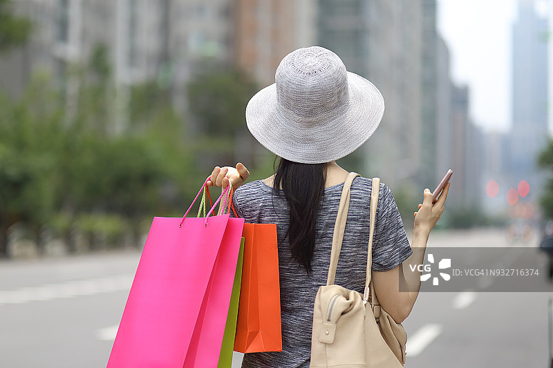 在户外手持购物袋和智能手机的女人图片素材