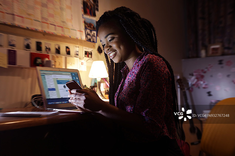 学生坐在房间的桌子旁，对着手机微笑图片素材