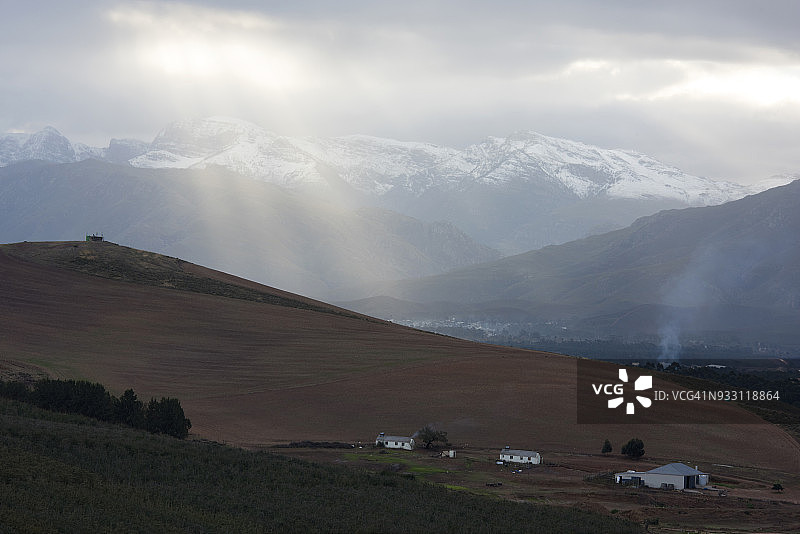前景中的奥维尔兹赫特农场，远处是格雷顿村，阳光穿透云层照耀着雪山，西开普省奥弗贝格图片素材