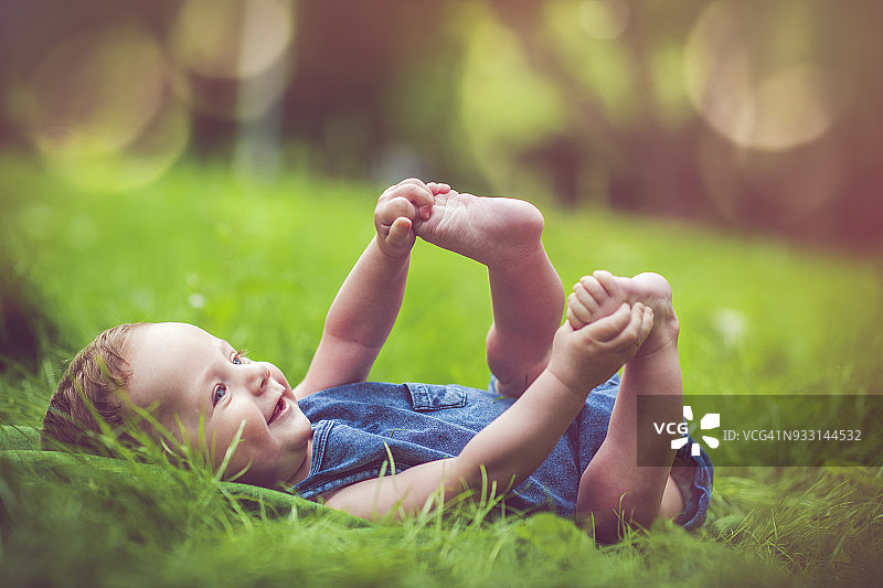 在草地上玩自己腿的可爱宝宝图片素材