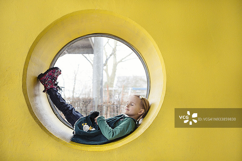靠在黄色墙壁圆形窗户内的女孩（4-5岁）图片素材