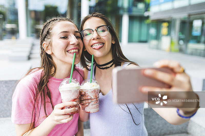两个快乐的少女在城市里喝奶昔自拍图片素材