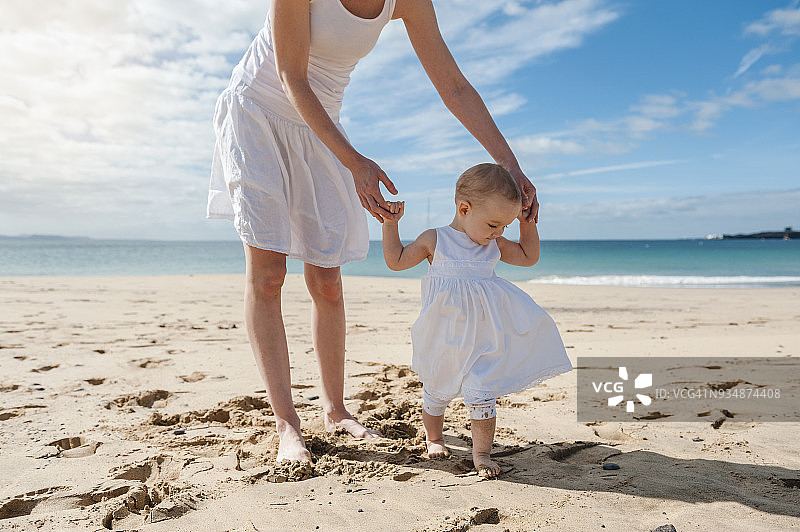 母亲帮助小女儿在沙滩上行走图片素材