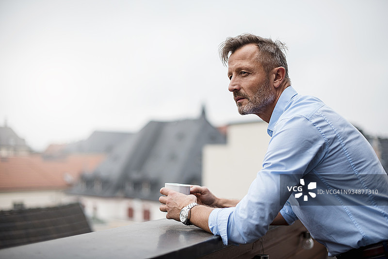 在屋顶露台手持咖啡杯的成熟商人图片素材