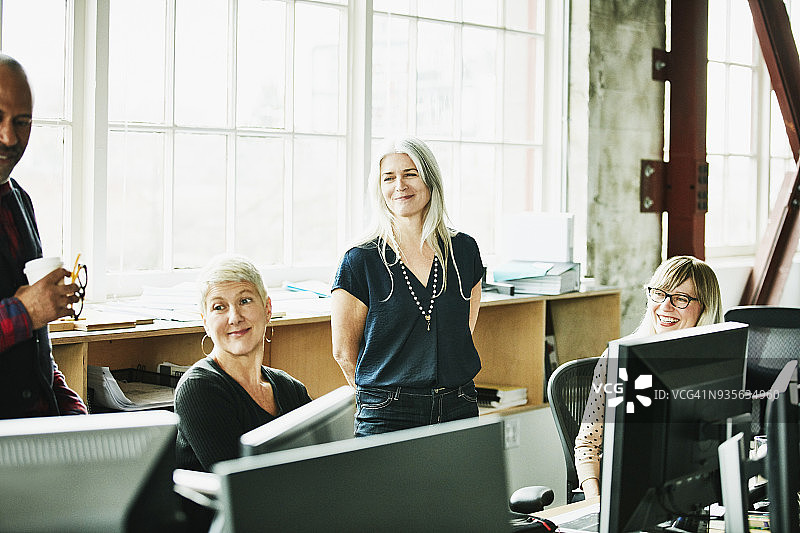 在设计办公室工作站，微笑的同事们举行非正式会议图片素材