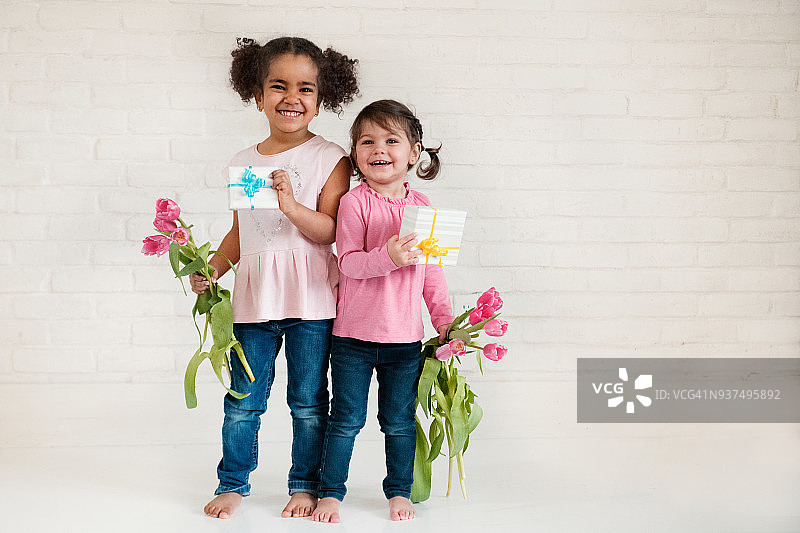 两个不同种族的小女孩拿着礼物和郁金香庆祝母亲节图片素材